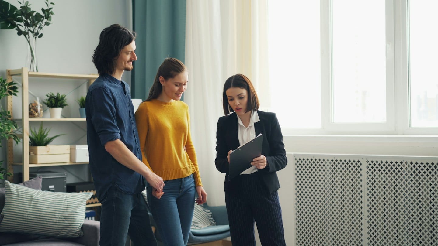 Agente immobiliare mostra documenti a una coppia in un appartamento moderno.